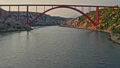 Amplia-Toma-Aérea-De-Un-Gran-Puente-Rojo-En-Un-Hermoso-Paisaje-Montañoso-Al-Atardecer,-La-Cámara-Avanza-Hacia-Arriba