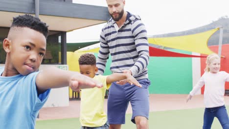 un maestro masculino diverso y escolares felices haciendo ejercicio en esteras en el patio de recreo de la escuela