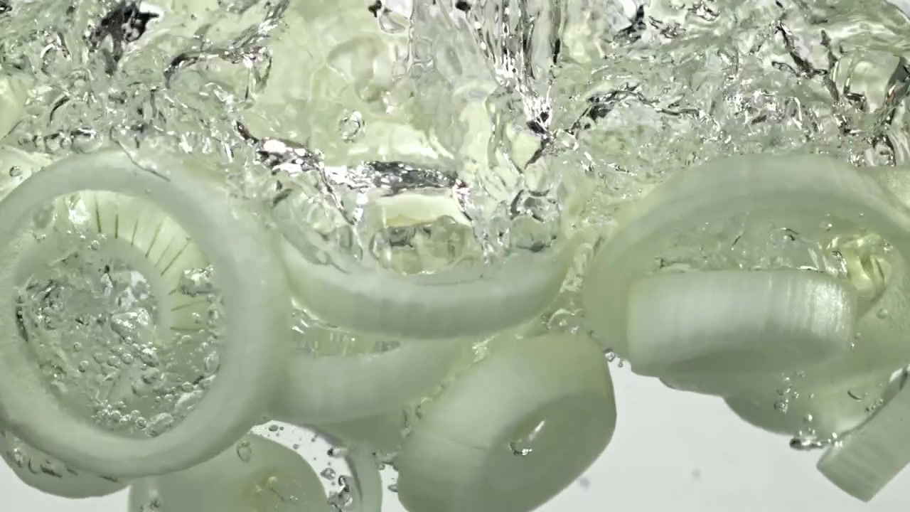 Anelli di cipolla freschi che cadono nell'acqua al rallentatore