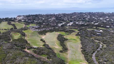 Drone captures sweeping aerial view of golf course, residential area, and coastline under daylight
