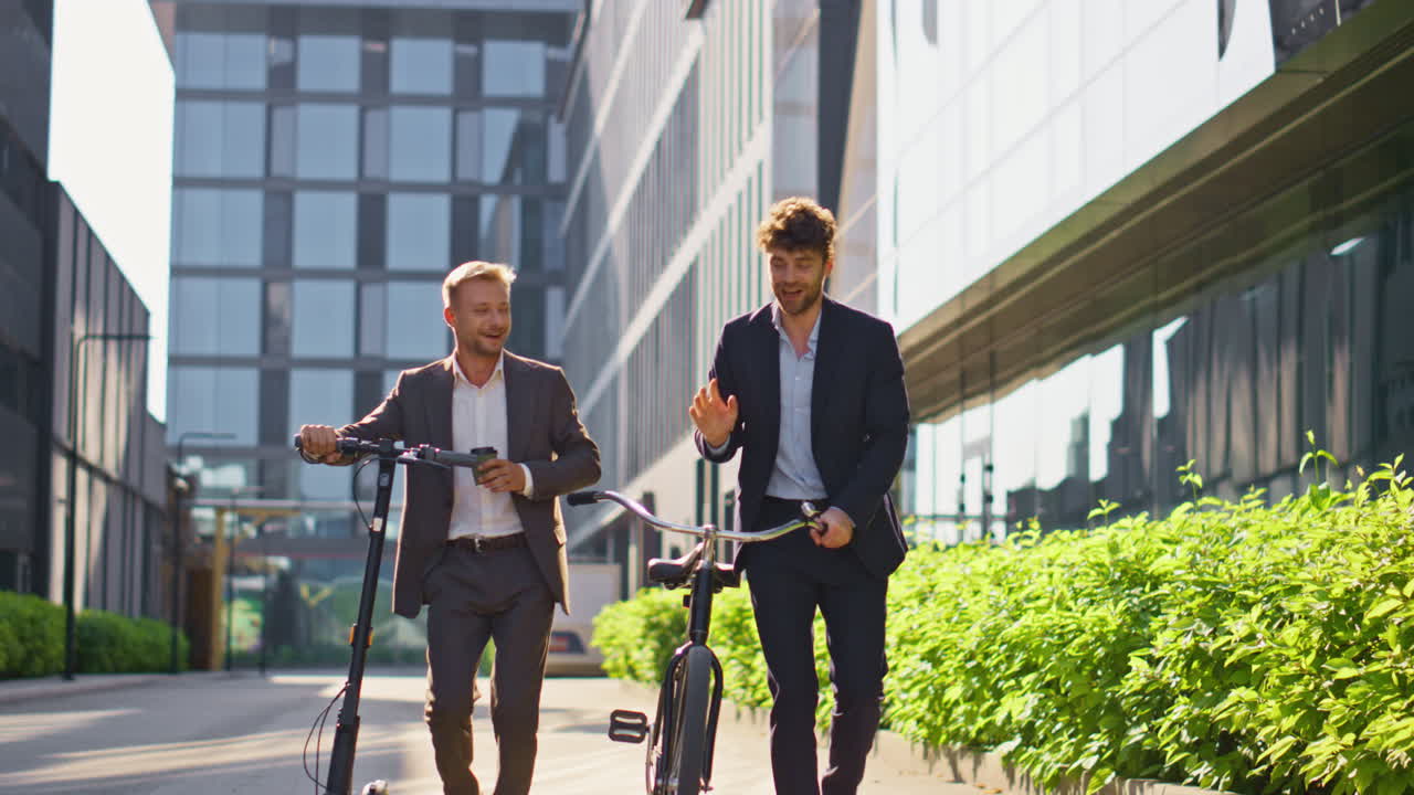 Two businessmen going city downtown. Smiling colleagues talking holding scooter