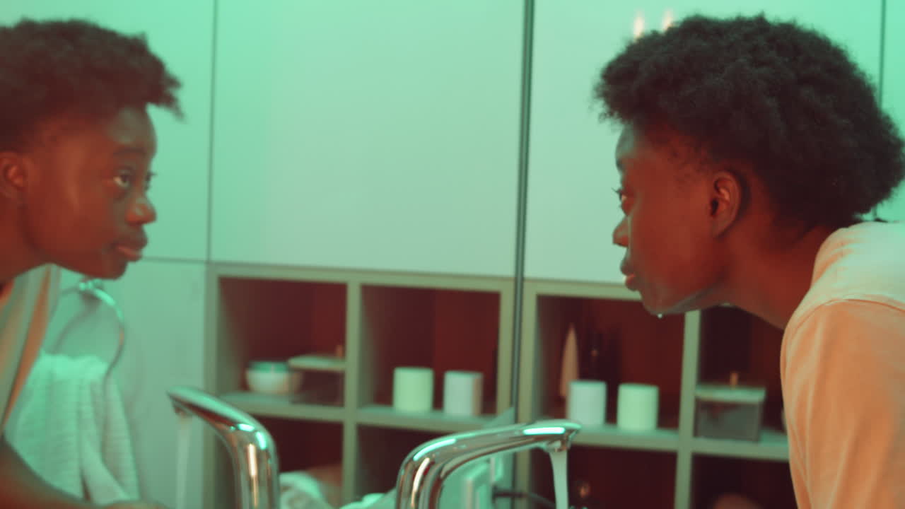 Donna afroamericana che si lava il viso al lavandino del bagno