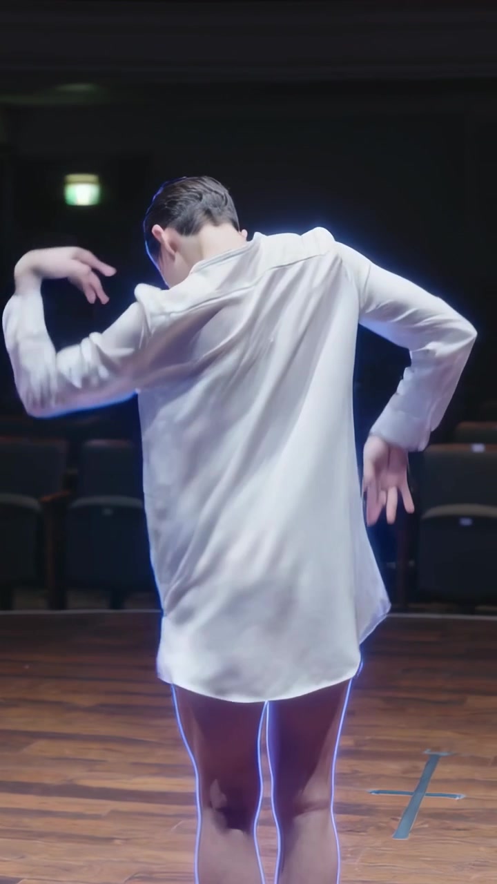Vídeo vertical: Dançarino solo começando a executar uma frase de dança no palco, com camisa branca e fita azul.