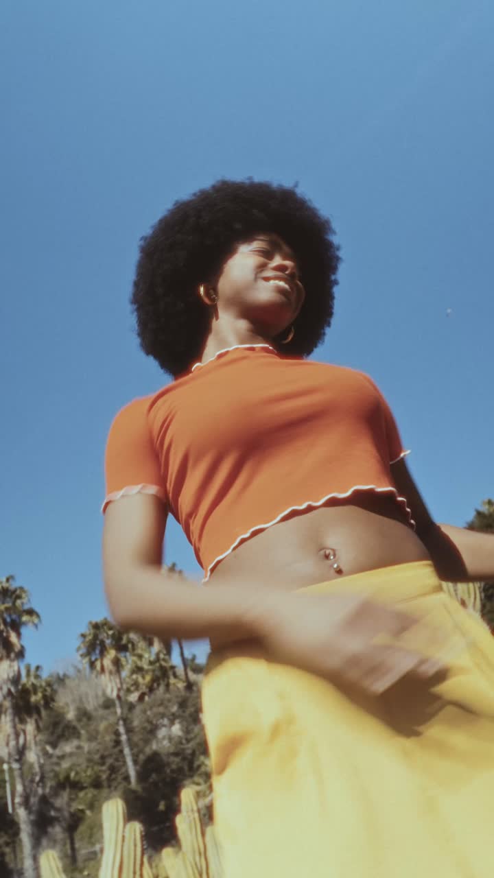 Giovane donna di colore gioiosa con afro che balla all'aperto in una giornata di sole