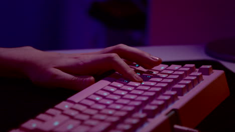 persona escribiendo en un teclado de juego rosa en una habitación oscura
