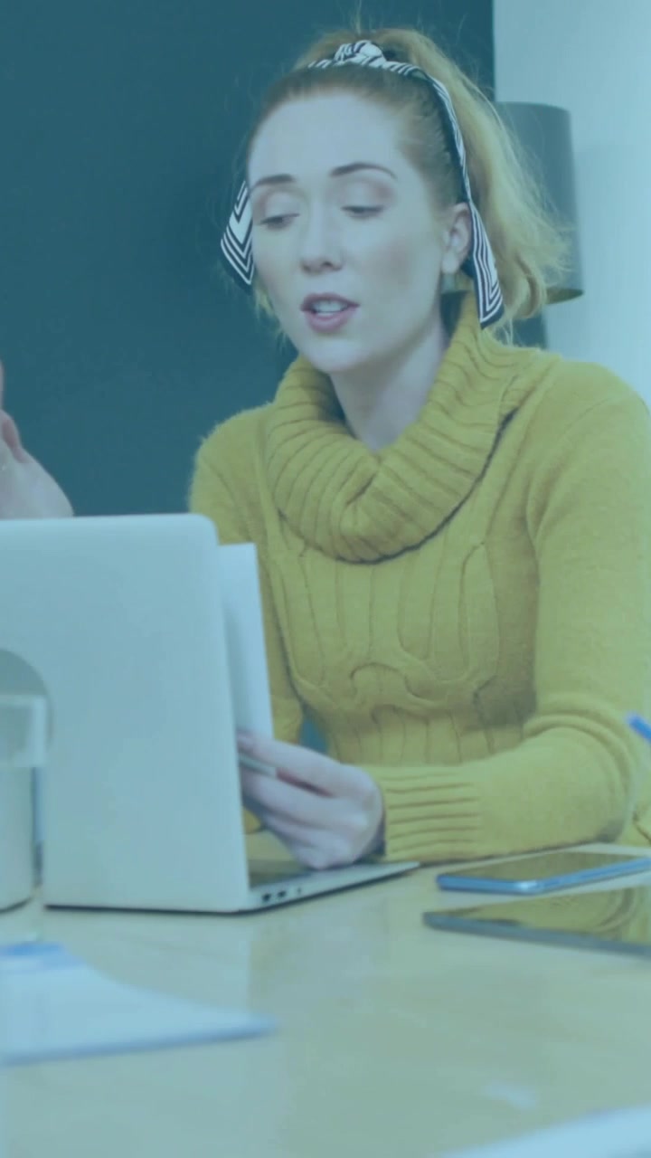 Vídeo vertical: Mulher lendo um documento enquanto fala, com HUD sobrepondo laptop e mesa em reunião de tecnologia.