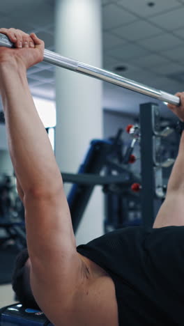 close-up of heavy barbell in man's hands during workout. muscular athlete lifting barbell up to build his arms muscles in sports club. vertical video