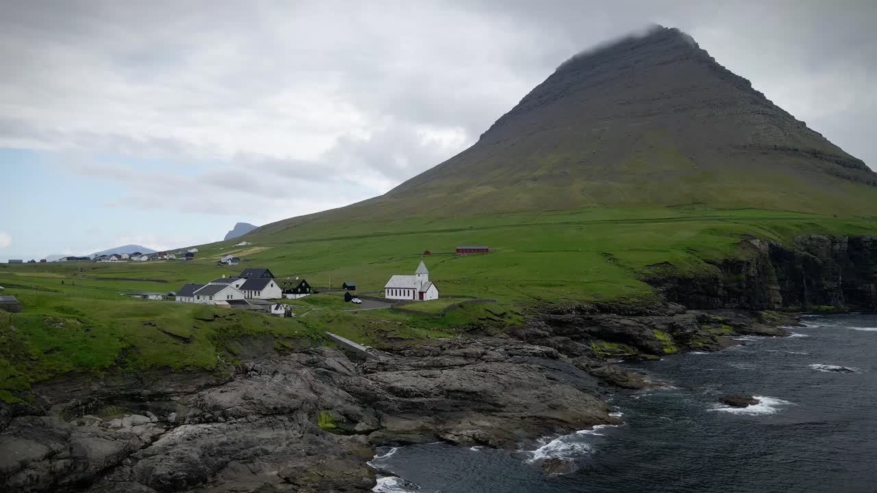 vista panorámica de viðareiði, las islas feroe, con un pintoresco pueblo costero con edificios encalados y una iglesia, situado contra una alta montaña envuelta en niebla y escarpados acantilados oceánicos