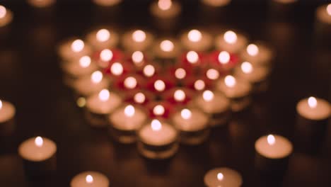 pull focus shot of romantic red and white candles in the shape of a heart on black background