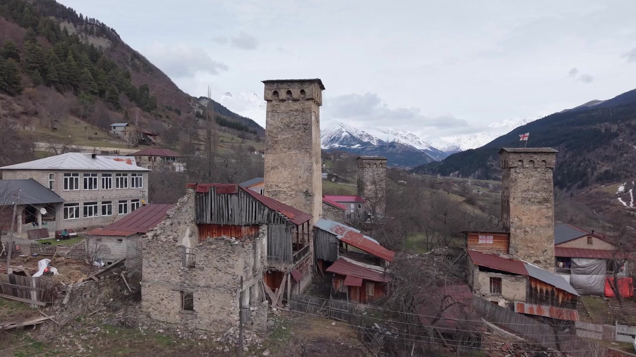Filmagem de drone com teleobjetiva capturando uma icônica torre Svan medieval em Mestia, lindamente emoldurada pelas majestosas Montanhas do Cáucaso cobertas de neve e pela deslumbrante paisagem alpina de Svaneti.