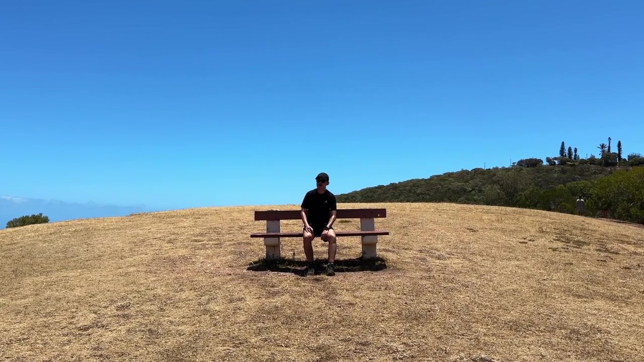 Uomo seduto su una panchina del parco in una giornata di sole con cieli azzurri in Nuova Caledonia.