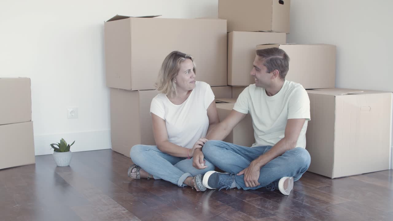 Cheerful couple sitting on floor near heap of boxes