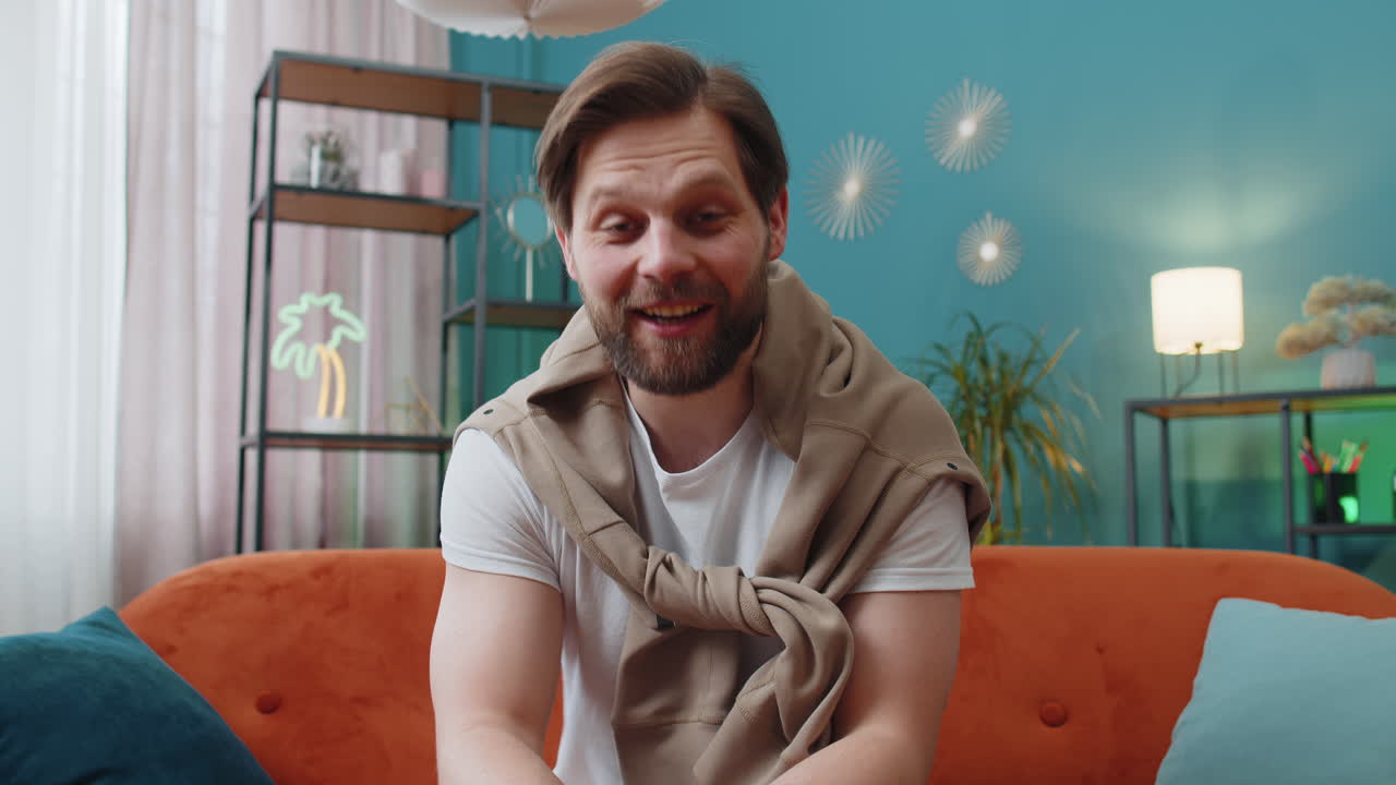 Caucasian man sitting on home couch looking at camera making video online webcam conference call