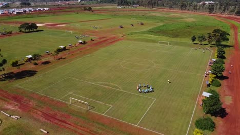 toma de avión no tripulado cinematográfico del calentamiento del equipo en un campo de fútbol verde por la tarde, por suelos arcillosos