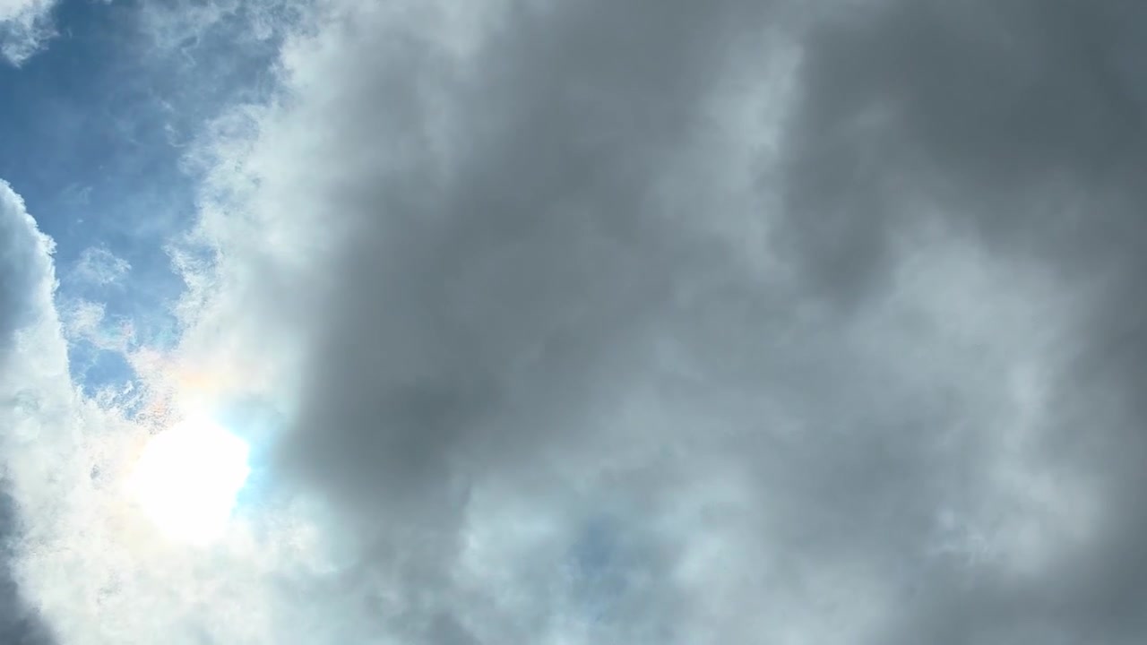 Dark dramatic storm clouds moving across a bright blue sky with the sun shining through