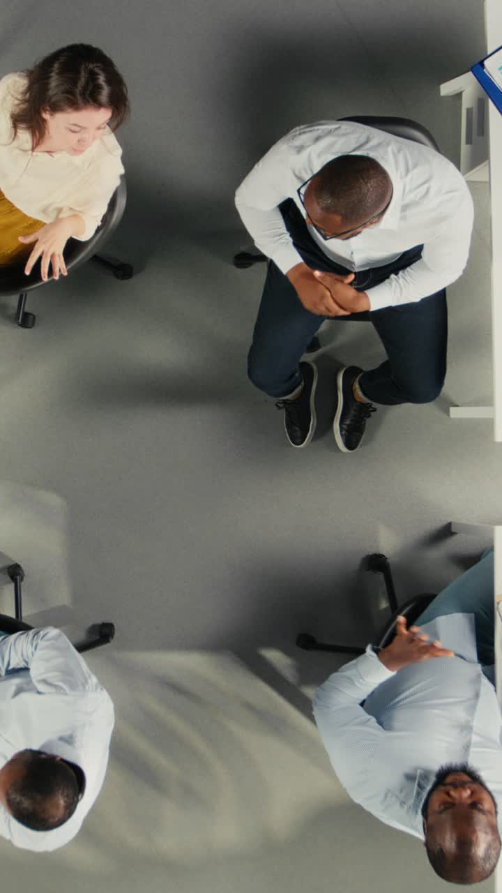Vertical Video Top down view zoom out of colleagues sharing reports and visual data
