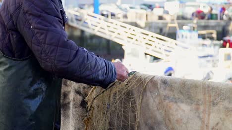 slow motion close up of a fisherman untangling fishing net in port at day time