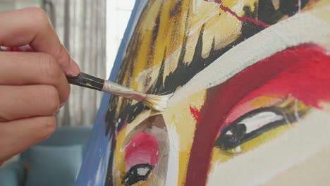 close up of a hand holding paintbrush mixed colour and painting a girl's forehead on the canvas