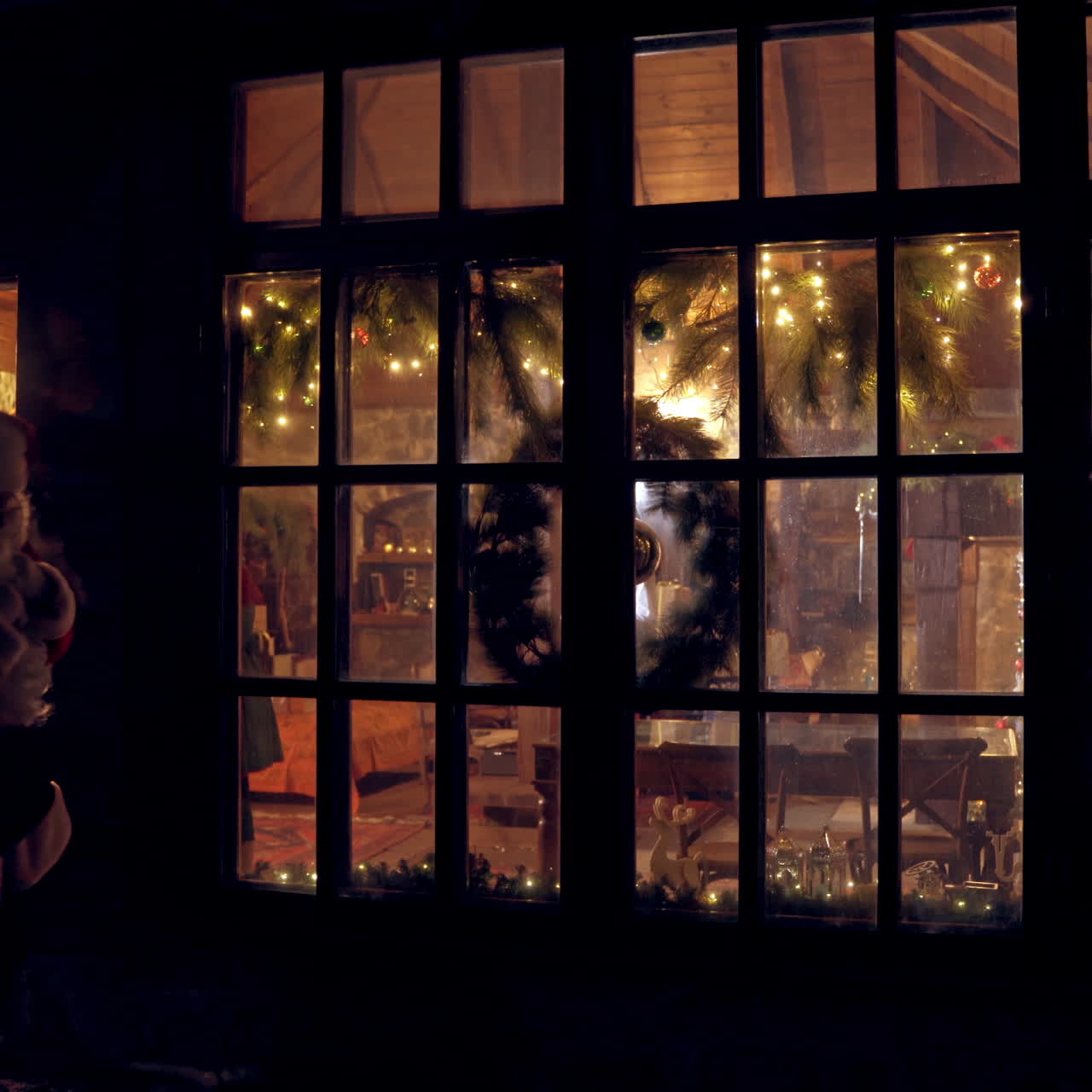 Christmas time. Santa with bag full of presents comes out of his residence. Santa in red costume is going to children at Christmas night. View from outdoors.