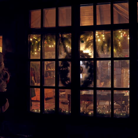 christmas time. santa with bag full of presents comes out of his residence. santa in red costume is going to children at christmas night. view from outdoors.