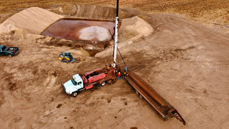men piling the pipes attached to the hook of a truck. workers dismantling equipment for boring gas or oil. drone footage distancing from the location.