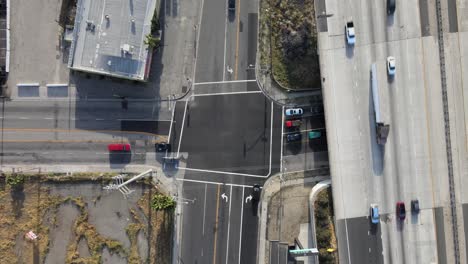 static drone view of an x-intersection beneath a highway bridge, capturing the onset of rush hour and long day-end shadows