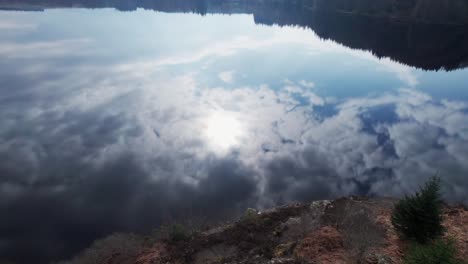 aerial tilting mirroring clouds and sun of sky in pure water of tranquil loch lochy lake in spean bridge, scotland, water reflection of cloudscape drone