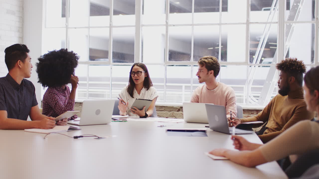 Coworkers sitting at a table in a meeting room listening to female manager, selective focus
