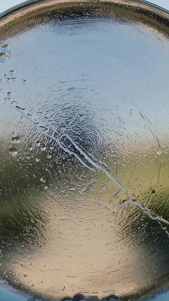 Video verticale: Disco che forma increspature e goccioline sui ciottoli, strato sottile che si scioglie creando un ruscello.