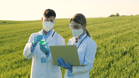 caucasian female and male researchers holding test tube with chemicals pesticides and using laptop in the green field