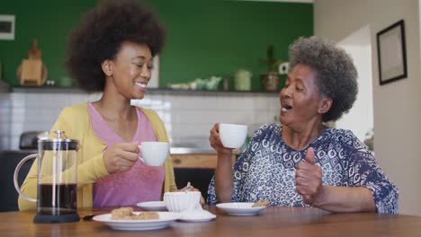 Happy-african-american-adult-daughter-and-senior-mother-drinking-coffee,-slow-motion