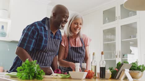 feliz pareja senior diversa usando delantales y cocinando en la cocina