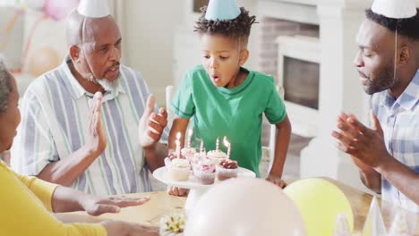 happy african american family celebrating birthday, son blowing out candles on cakes, slow motion
