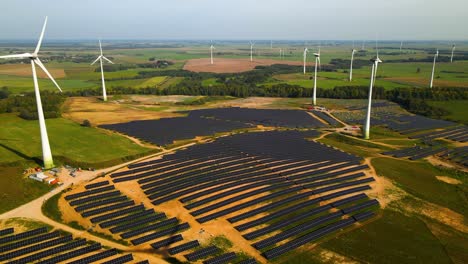 Luftaufnahmen-Von-Solaranlagen-Und-Windturbinen-In-Einem-Windpark,-Der-An-Einem-Sonnigen-Tag-Auf-Einer-Weiten-Grünen-Wiese-In-Taurage,-Litauen,-Grünen-Strom-Erzeugt,-Beim-Herauszoomen