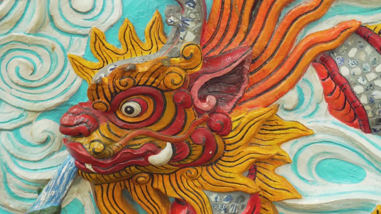 A colorful dragon sculpture showcases intricate details with vivid shades of red, orange, and gold against a blue background of sky and cloud, highlighting cultural artistry and design, Hanoi, Vietnam
