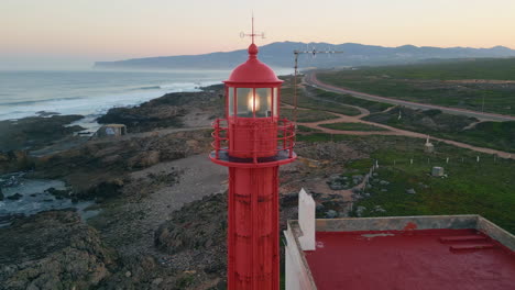 Drone view lighthouse shining on evening seashore. Red beacon blinking on coast