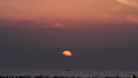 orange sun and sunset skies slow zoom out reveal of silhouette of people on karachi beach