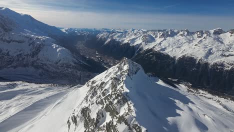 Una-Amplia-Vista-Aérea-De-Un-Impresionante-Paisaje-Alpino,-Que-Muestra-Una-Afilada-Cresta-Montañosa-Que-Conduce-A-Picos-Cargados-De-Nieve-Bajo-Un-Cielo-Despejado