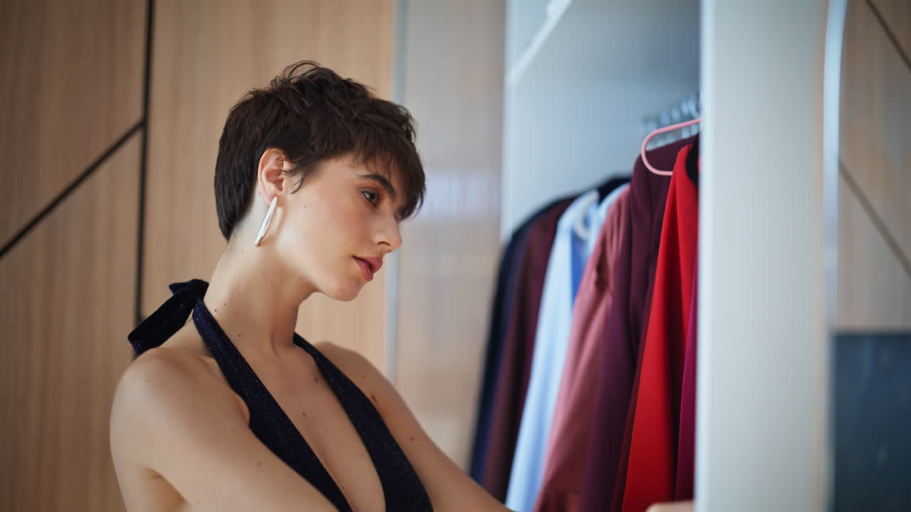 Primo piano di una donna nel guardaroba che esamina i vestiti, scorrendo gli appendiabiti. La donna sceglie il suo outfit.