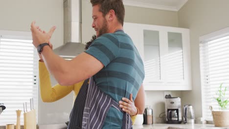 video de una feliz pareja diversa bailando en la cocina con delantales