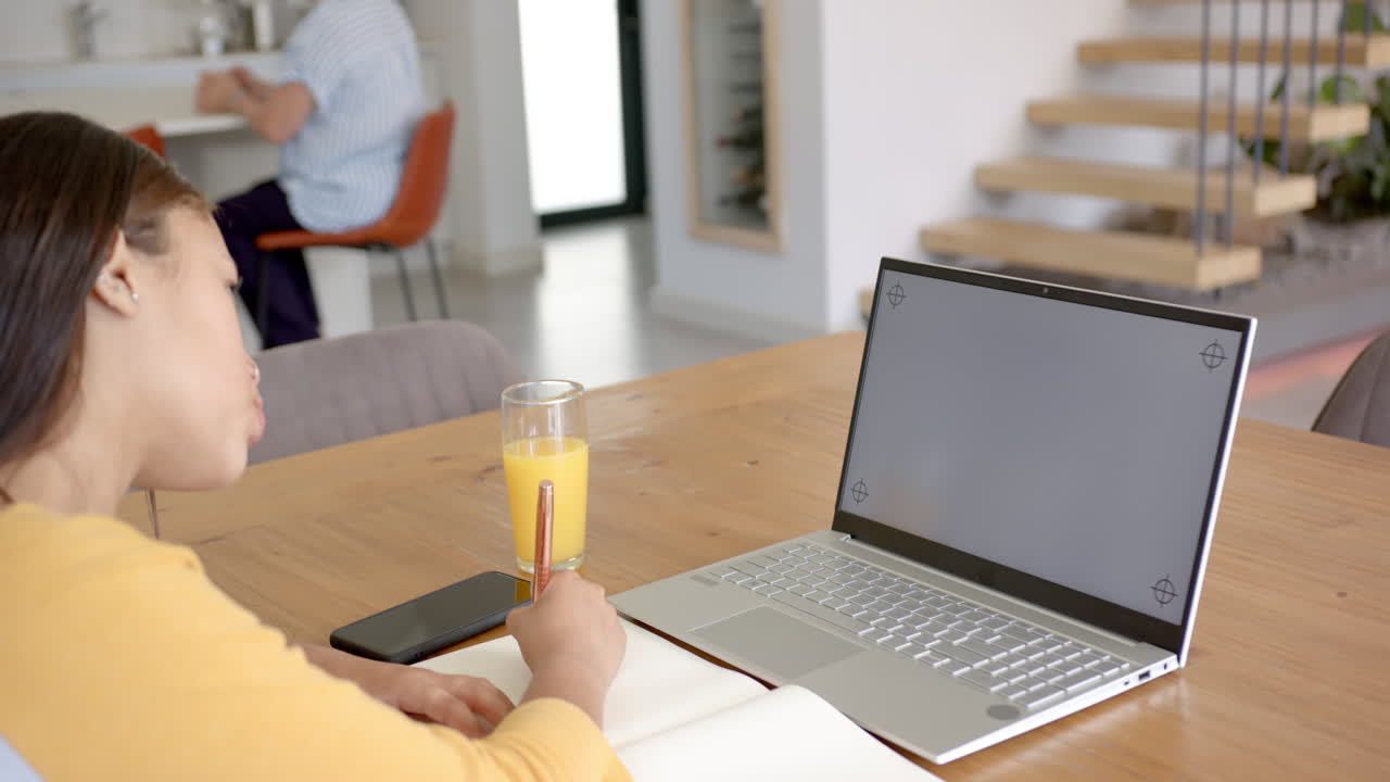 Writing in notebook, asian woman sitting at table with laptop and glass of juice, copy space