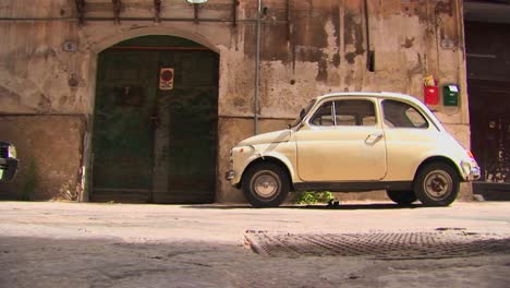 Un-Pequeño-Coche-Aparcado-Fuera-De-Un-Antiguo-Edificio-De-Piedra-Palermo-Italia