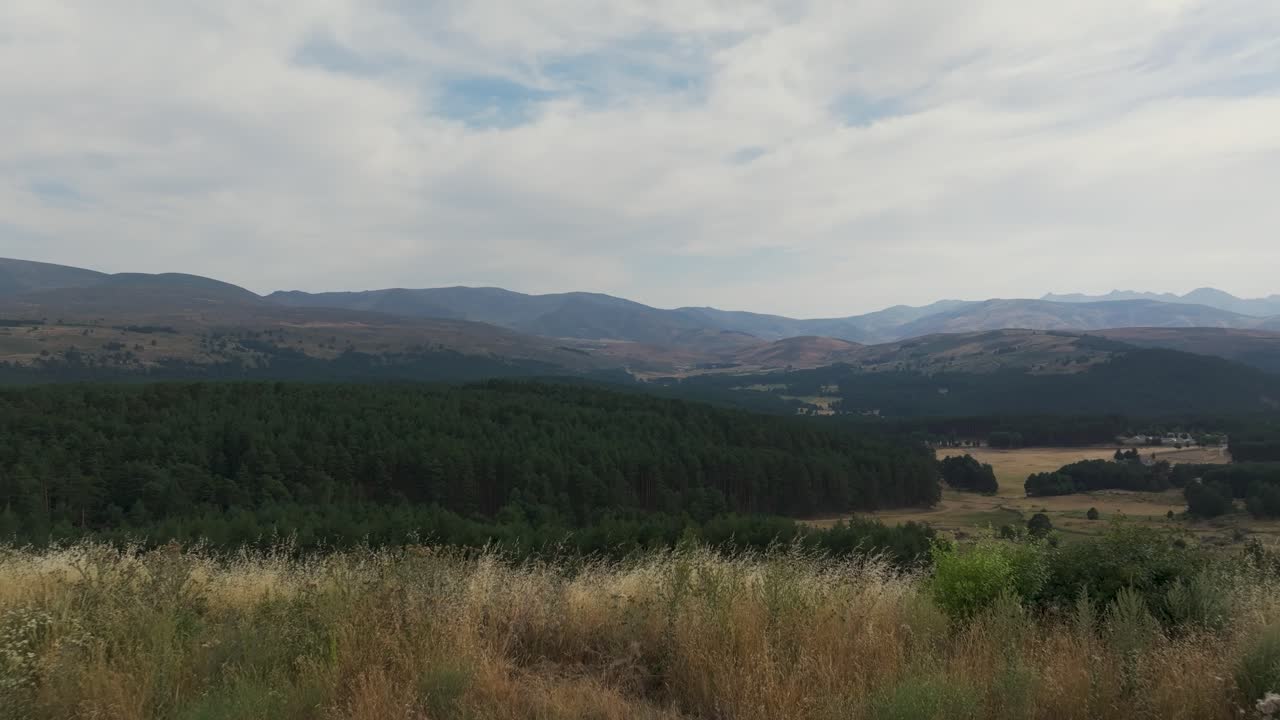 vuelo frontal con un dron comenzando desde una plataforma de tierra sólida y descubrimos un paisaje fascinante del sistema montañoso de la sierra de gredos en ávila con sus bosques exuberantes, el cielo tiene nubes