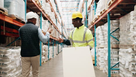 two warehouse workers laughing while pushing a box cart down a warehouse aisle