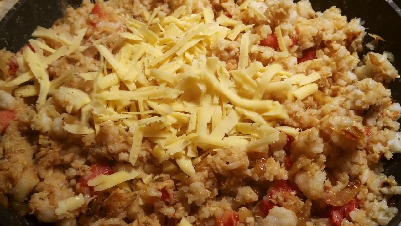 Static view of grated cheese being sprinkled over fried rice with tomatoes, bell peppers and tuna