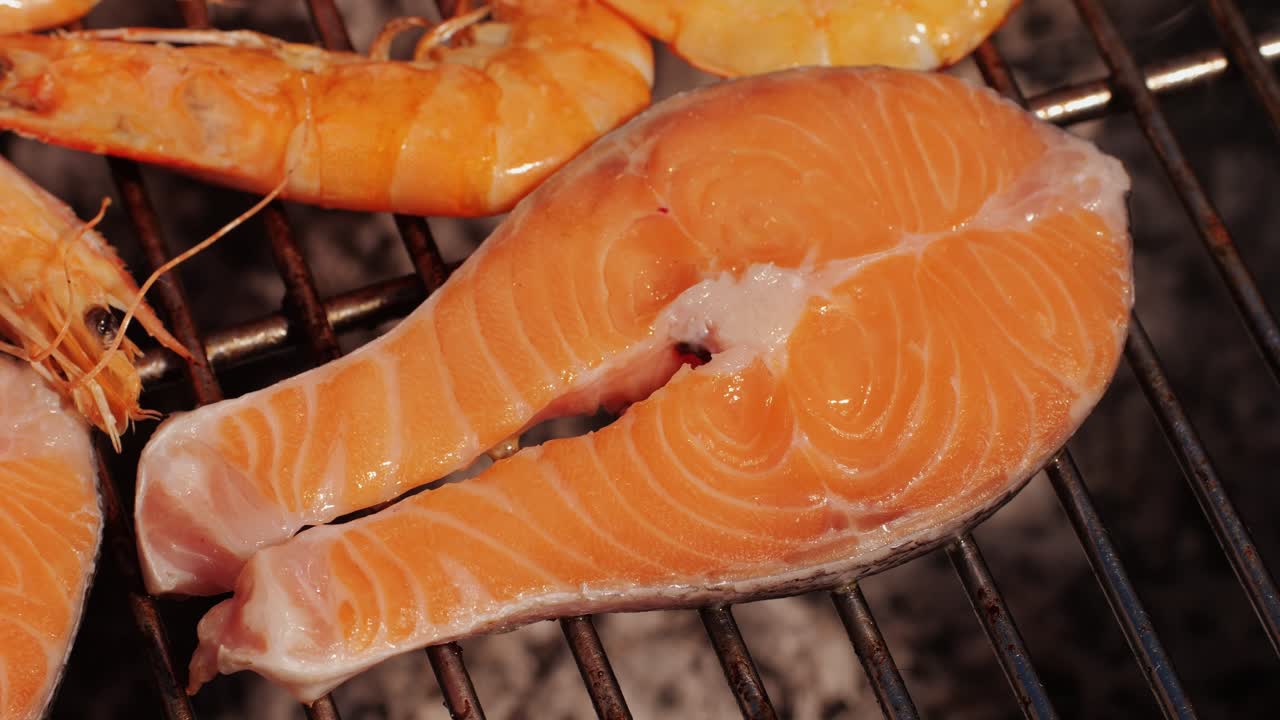 Chef cooking red salmon fish steaks with oil and spices on grill close-up. Prawns on fire throwing them on pan. Making Dorado fishes on frying grill. Restaurant Food concept. Sea food barbecue.