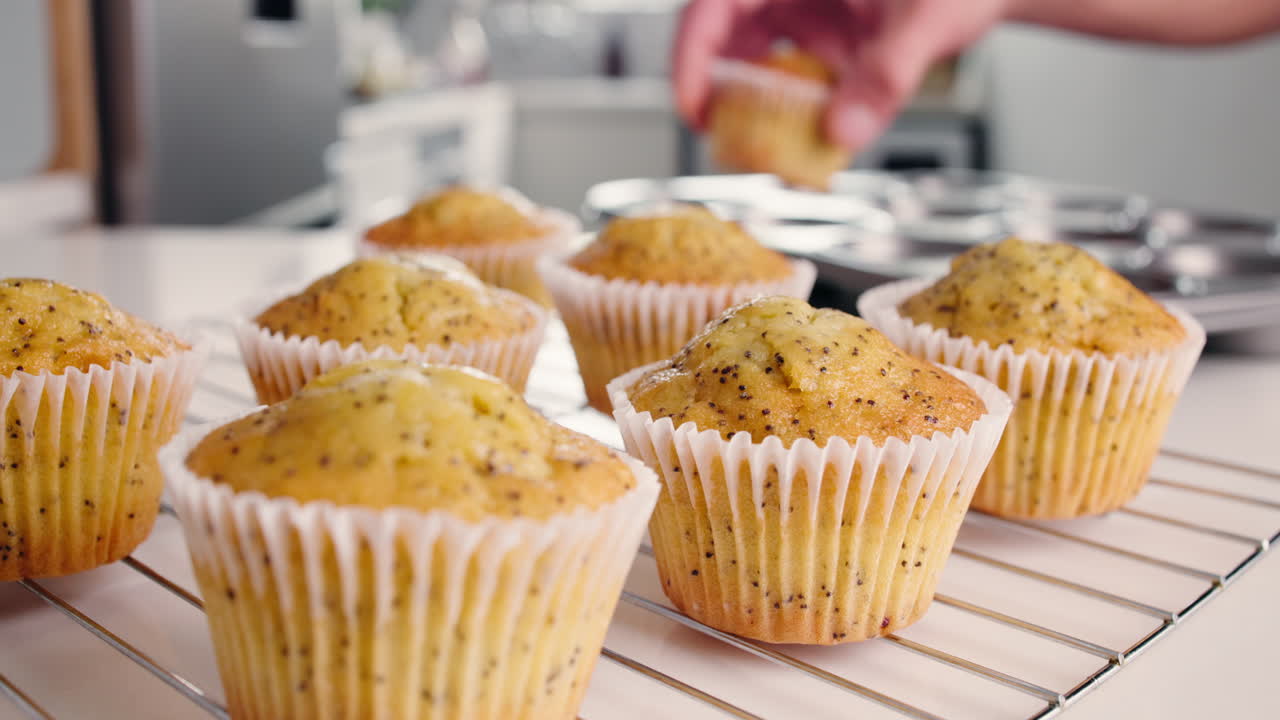 Una mano prende un muffin appena sfornato da una griglia di raffreddamento
