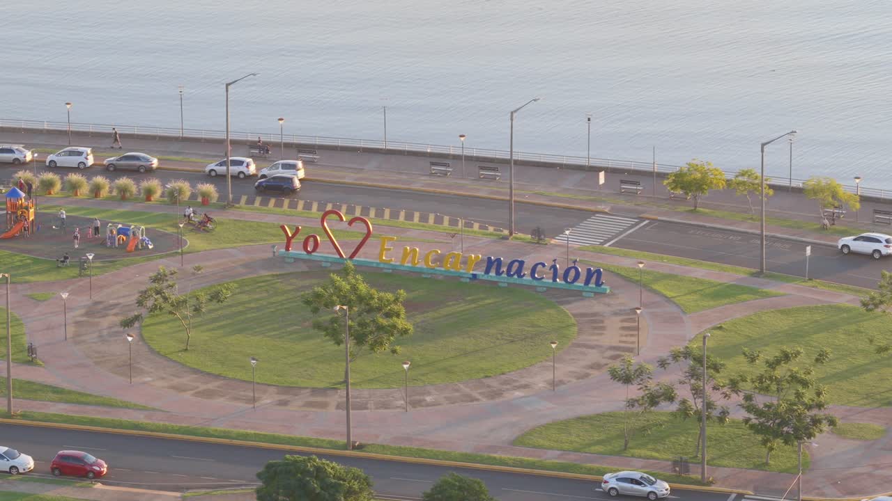 Close-up aerial view of the colorful "Yo love Encarnación" sign on the waterfront promenade (Costanera) in Encarnación, Paraguay, during golden hour.