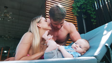 beautiful caucasian couple sit over their infant baby lying on deck chair. happy family of three on vacation. low angle view.