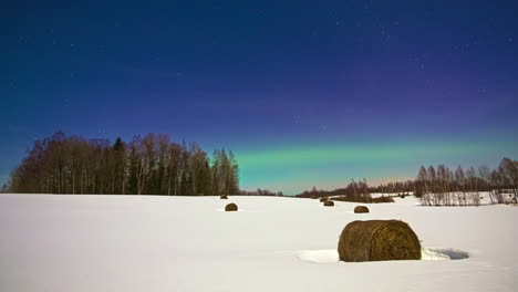 Impresionantes-Luces-Brillantes-De-Aurora-Boreal-Sobre-El-Cielo-Azul-Con-Estrellas-En-Un-Día-De-Invierno-Cubierto-De-Nieve-En-Un-Campo-Agrícola-Con-Pacas-De-Heno-En-Timelapse